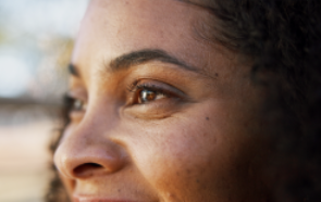 Close-up of a smiling person’s face, focusing on their eye, cheek, and curly hair in soft natural light. The blurred background conveys warmth and vulnerability, subtly reflecting themes related to psychiatric diagnosis.